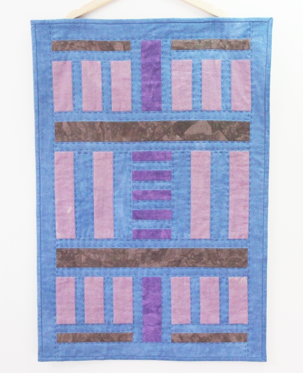 hand stitched quilt with geometric pattern hanging on wall