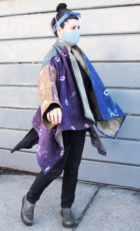 woman standing on sidewalk wearing colorful patchwork quilt coat and face mask