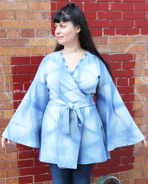 woman wearing blue wrap shirt with big flowing sleeves standing in front of brick wall