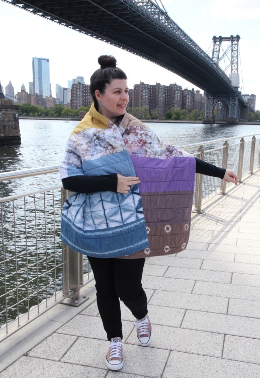 woman wearing a colorful patchwork hand dyed quilted shibori shawl, standing in front of the Williamsburg Bridge in Brooklyn